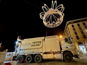 Camion aspiratrice Azur Aspi stationné sous une couronne lumineuse géante dans une rue la nuit.