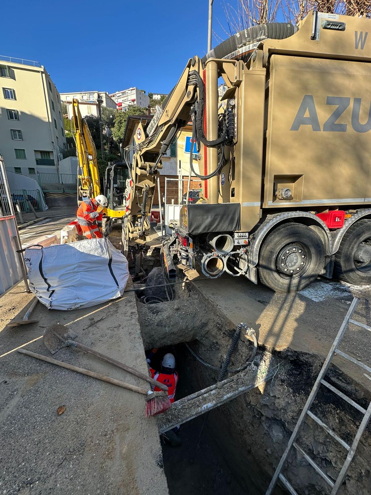 Travaux d'excavation : ouvriers dans une tranchée avec aspiratrice excavatrice Azur et équipements de chantier.