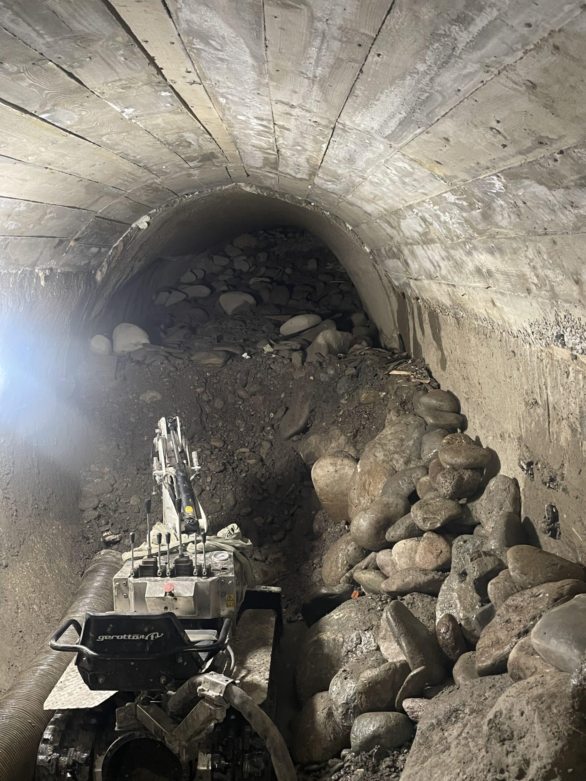 Excavateur Gerotto télécommandé déblayant des roches dans un tunnel voûté souterrain encombré.