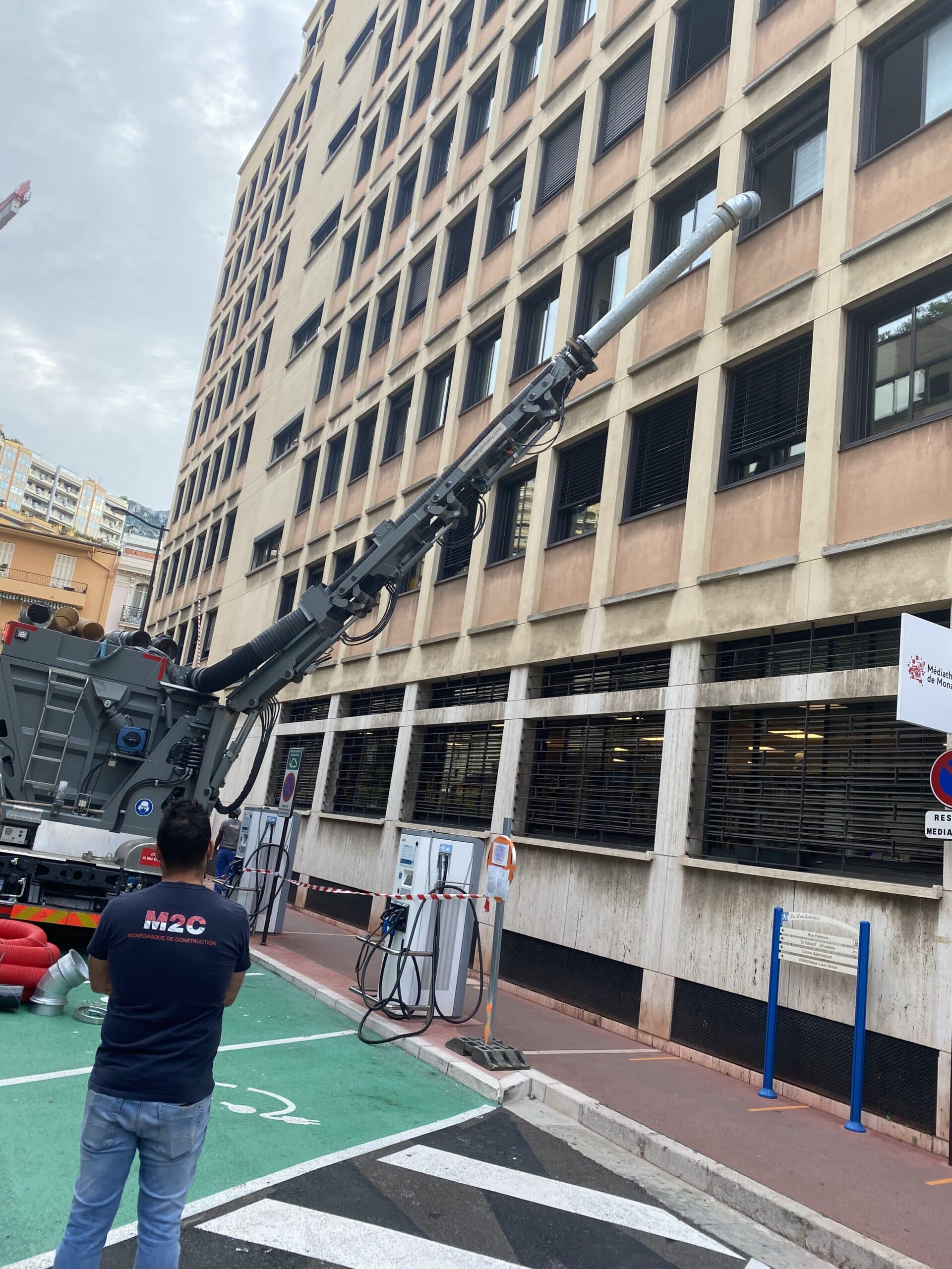 Camion aspirateur M2C avec bras articulé devant la Médiathèque de Monaco, travaux de construction urbaine.