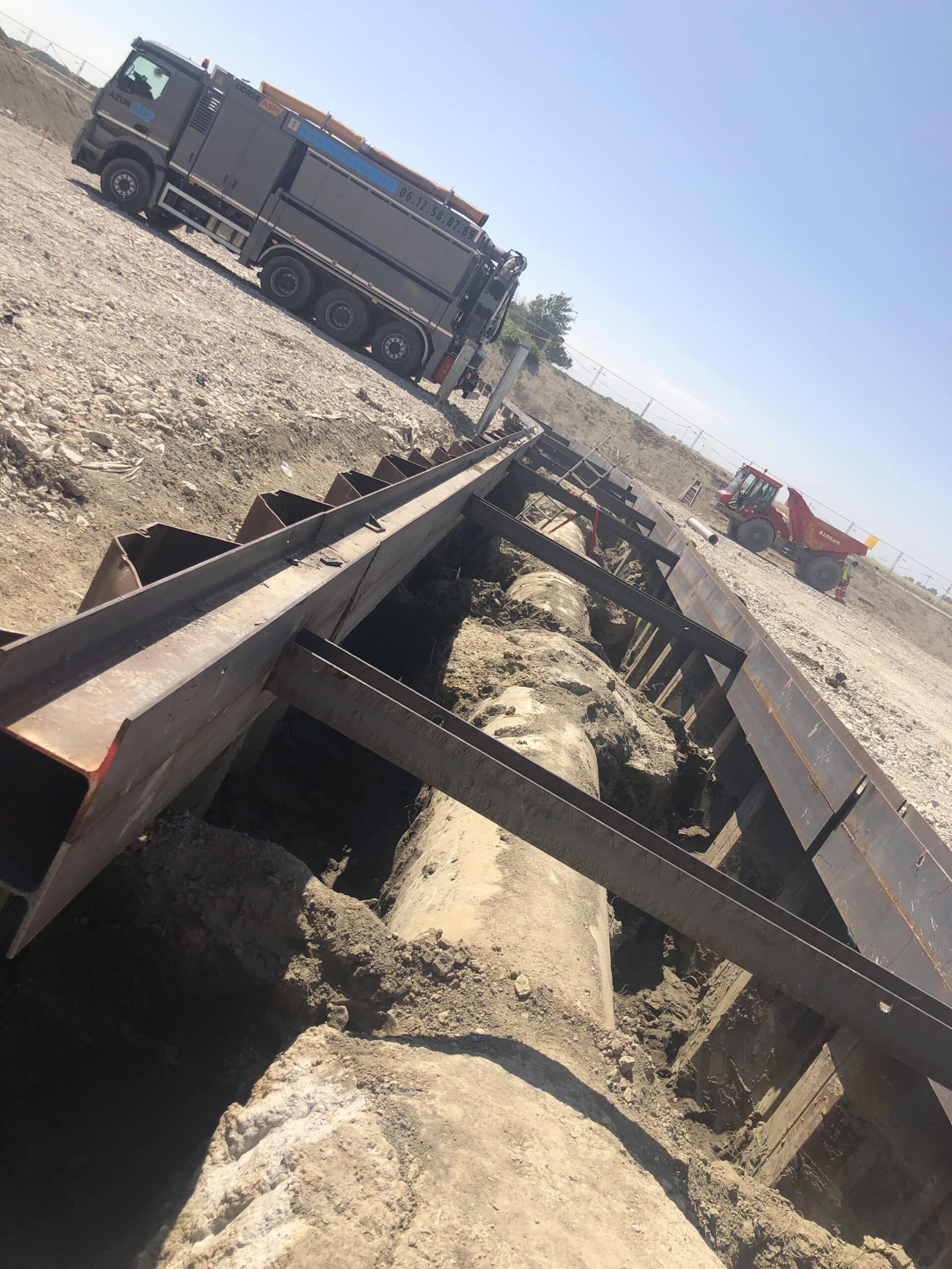 Camion Azur Aspi près d'une tranchée de canalisation étayée par du blindage métallique sur un chantier de travaux publics.