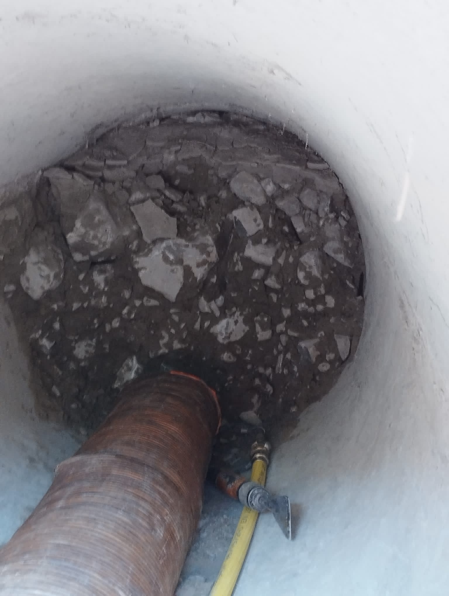 Débouchage d'une canalisation obstruée par des débris rocheux avec un tuyau d'aspiration et une buse de nettoyage.