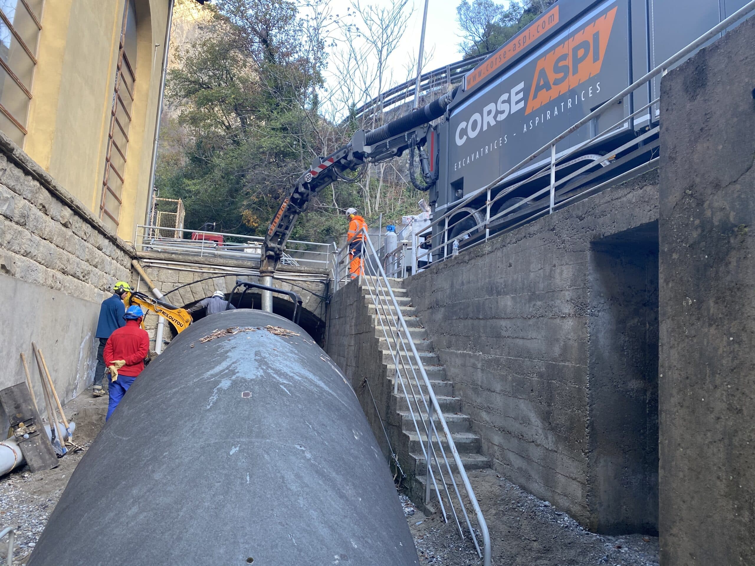 Camion Corse Aspi excavatrice-aspiratrice et ouvriers intervenant sur une canalisation massive sur un chantier.