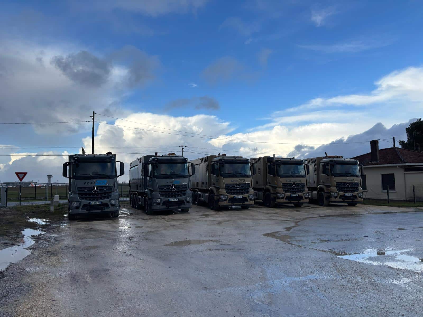 Flotte de camions aspiratrices excavatrices Mercedes-Benz AZUR ASPI stationnée sur un terrain humide.
