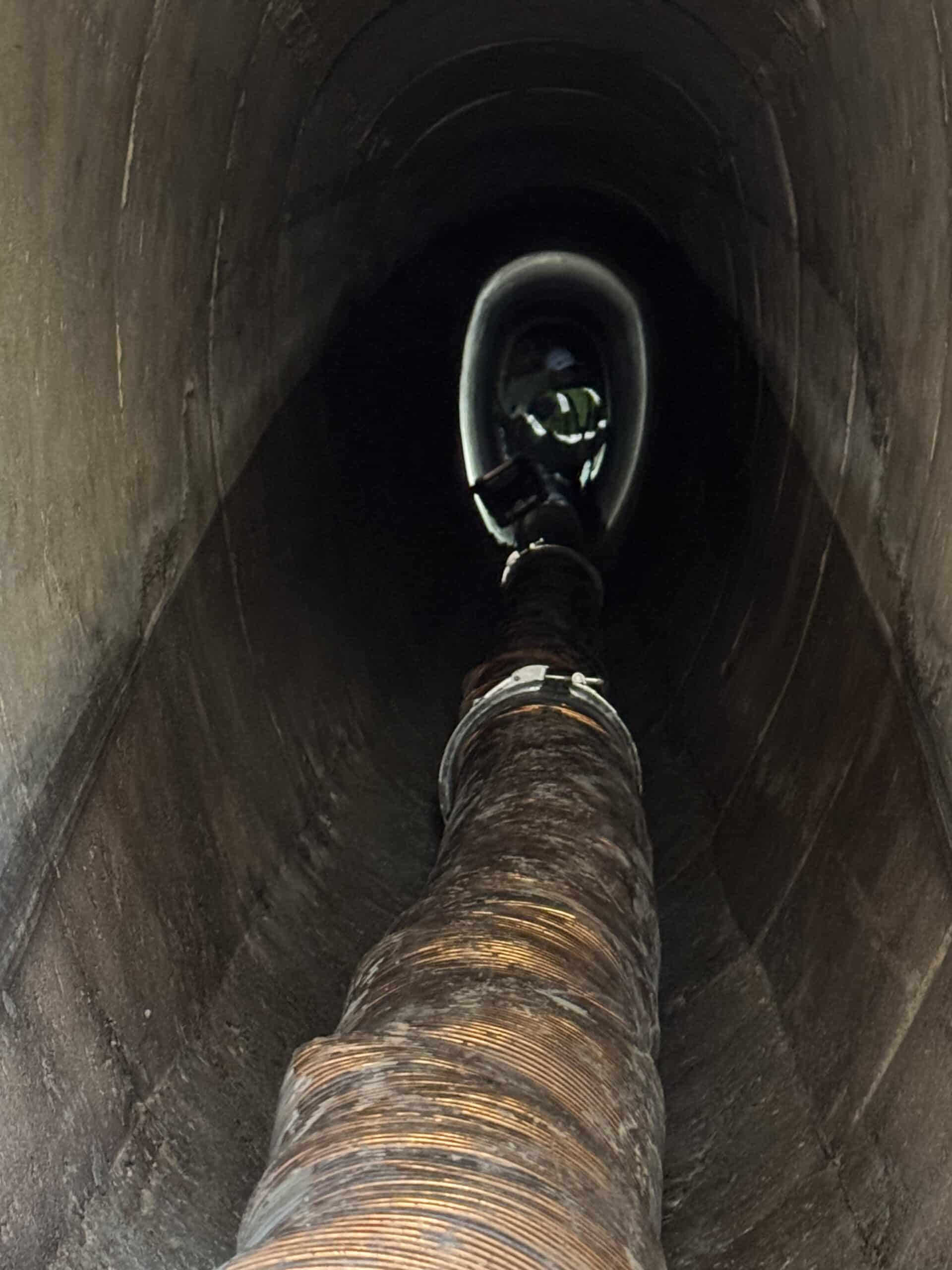 Conduit flexible métallique inséré dans une canalisation circulaire sombre menant à une ouverture technique éclairée.