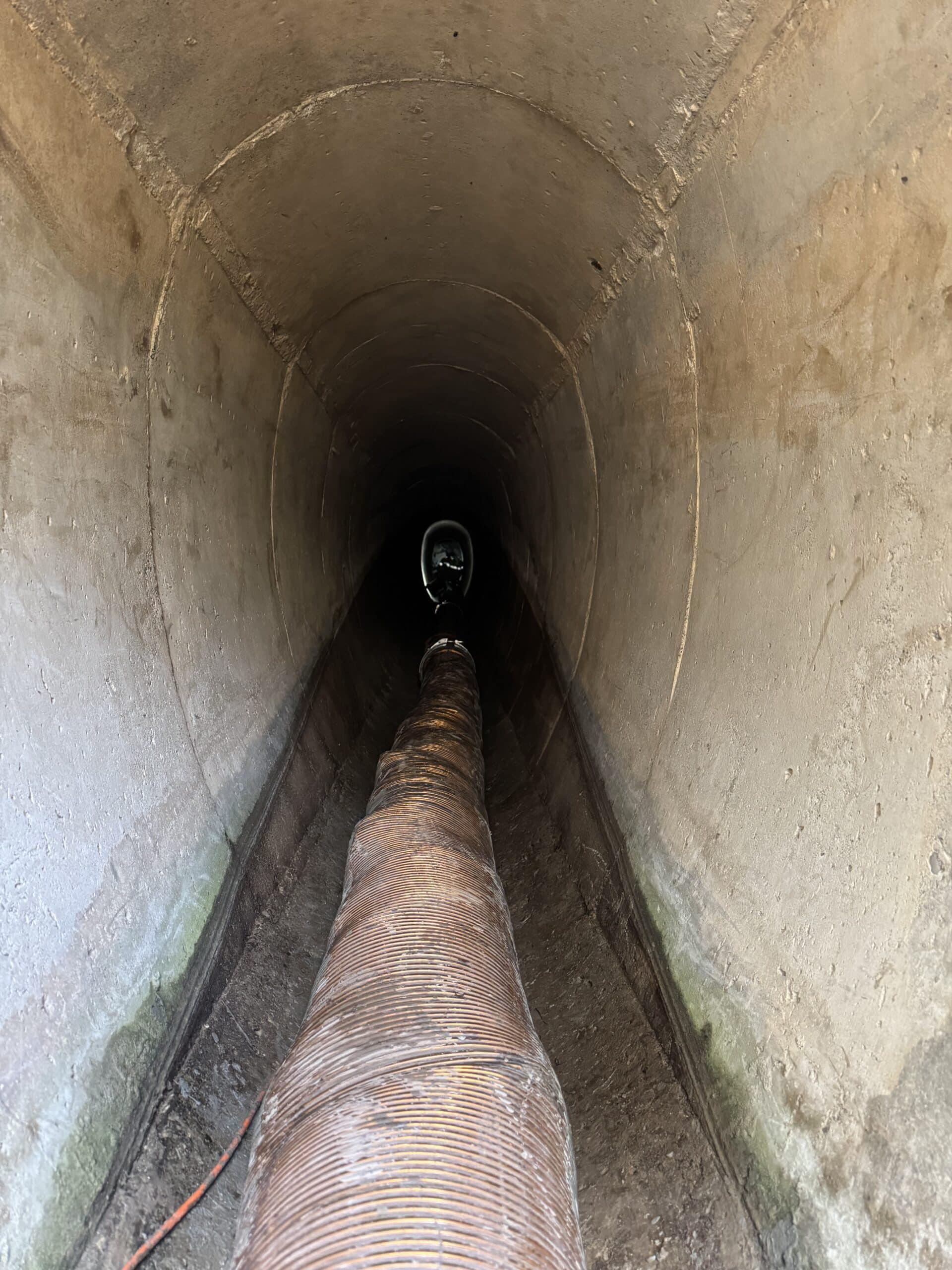 Tuyau flexible nervuré dans un tunnel en béton sombre avec une source lumineuse au loin pour inspection.