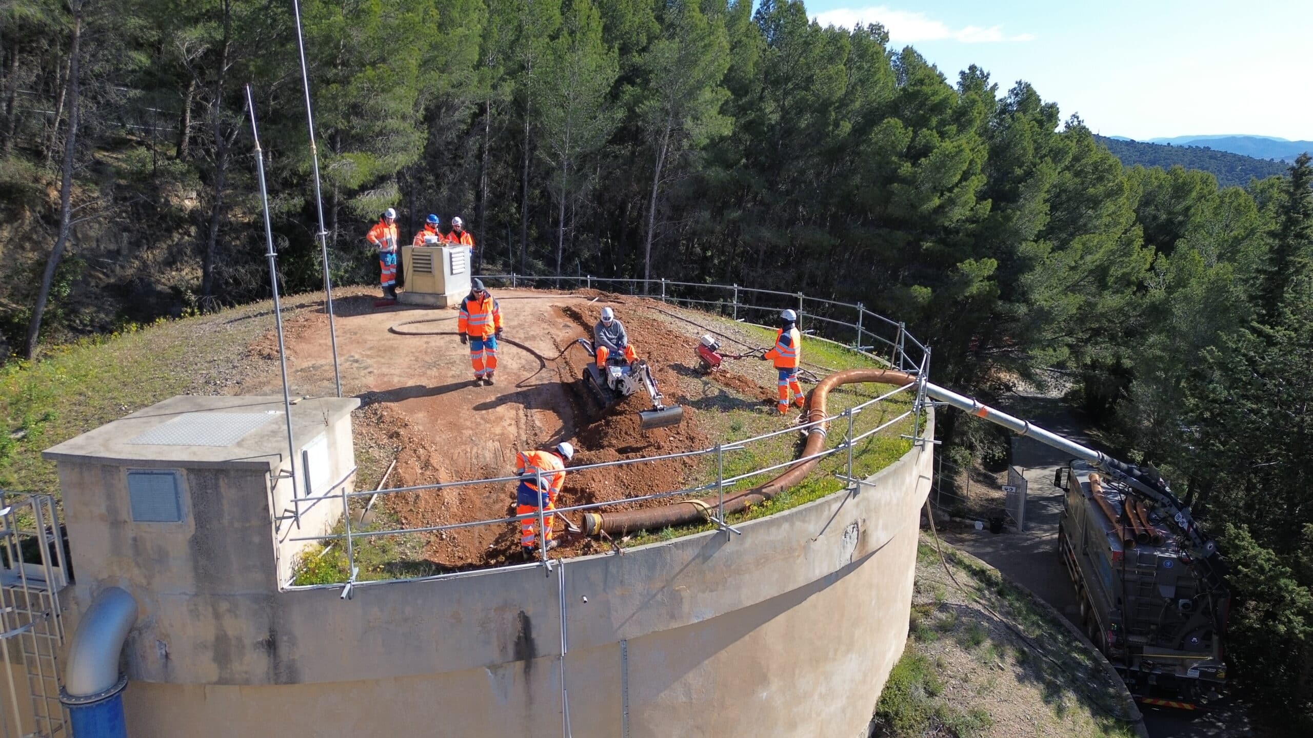 Ouvriers en tenue de sécurité effectuant la maintenance d'un réservoir d'eau avec excavatrice et camion d'aspiration.