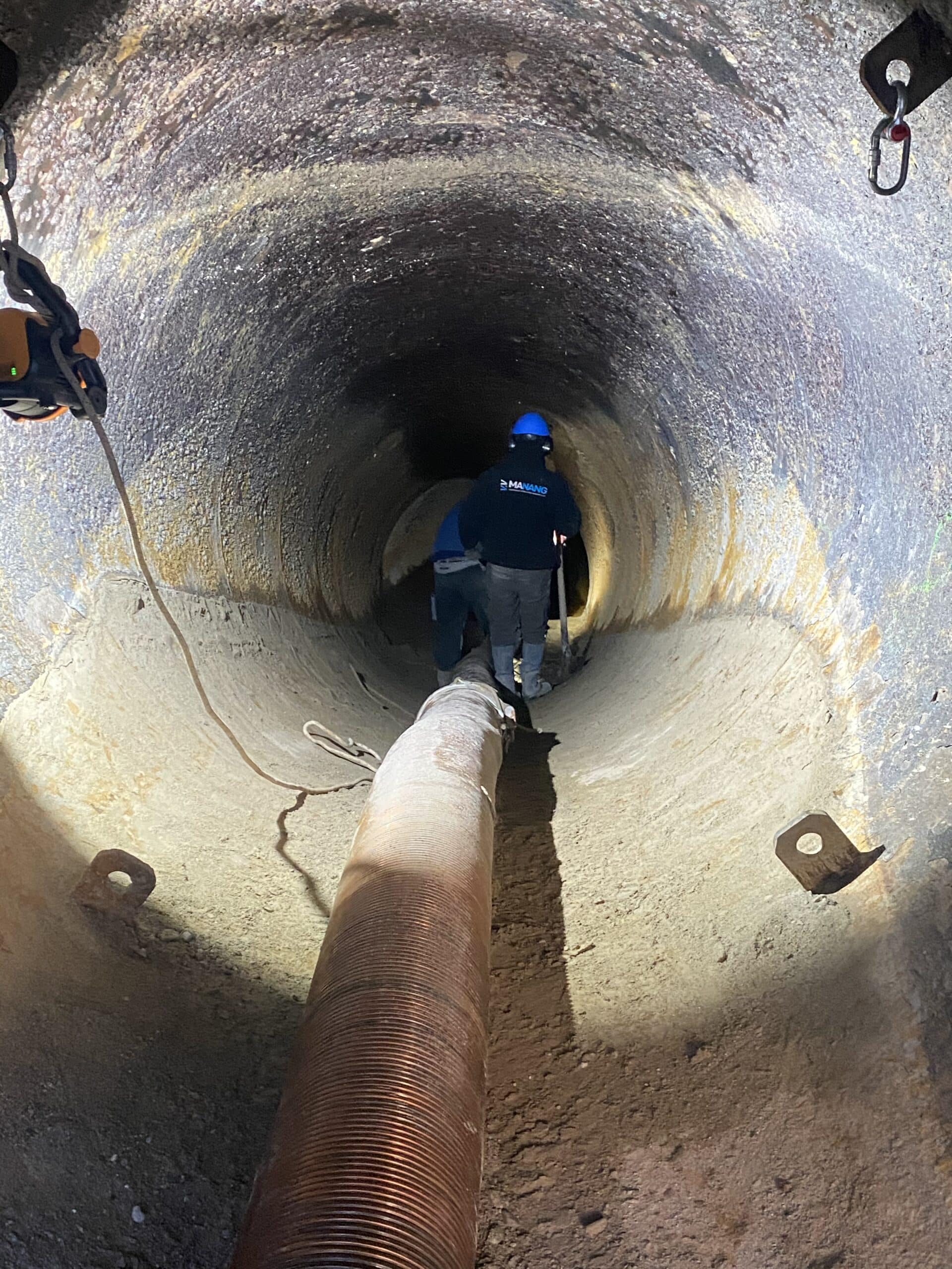 Ouvriers Manang travaillant dans un tunnel avec un gros tuyau flexible, éclairage de chantier souterrain.