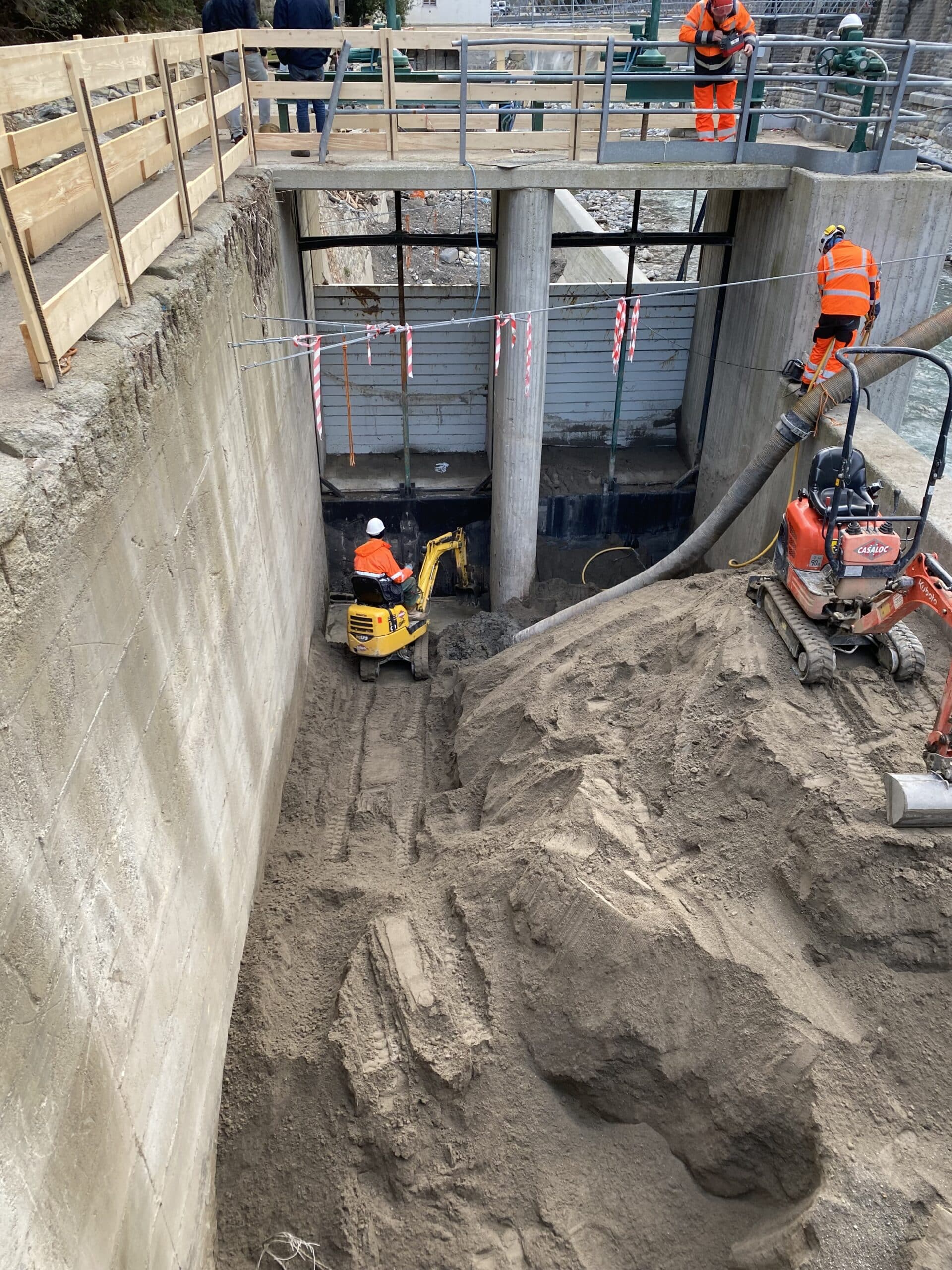Ouvriers et pelleteuses Casaloc excavant du sable dans une structure en béton avec vannes hydrauliques.